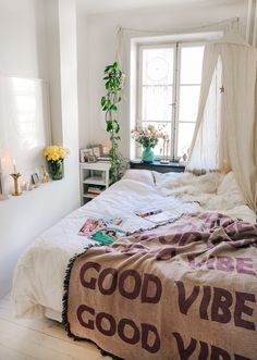 an unmade bed with a good vibe blanket on top of it next to a window