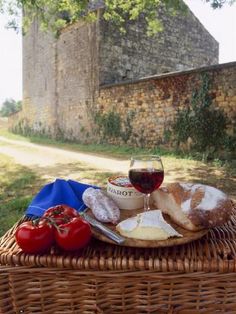 a wicker picnic basket with bread, cheese and tomatoes on it next to a glass of wine