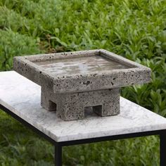 a cement container sitting on top of a white marble table in front of some bushes