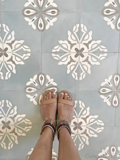 a woman's feet in sandals standing on a tile floor with white and gray designs