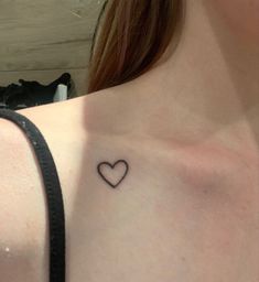 a woman's chest with a small heart tattoo on the left side of her chest