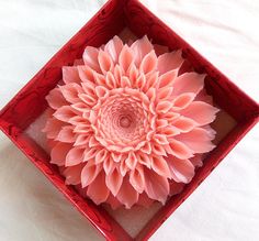 a pink flower in a red box on a white tableclothed surface with an intricate design