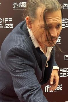 a man in a suit and tie holding a cell phone to his ear while standing next to a red carpet