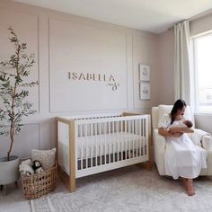 a woman sitting in a chair next to a baby crib with a tree on the wall