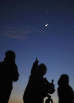 people are silhouetted against the night sky with an object in the distance, and one person is holding a camera