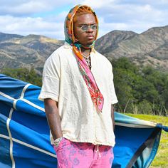 a man with dreadlocks standing in front of a blue tarp and mountains