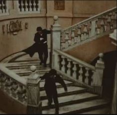 two people are walking up the stairs in an old fashion building, one is holding his coat