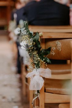 a bouquet of flowers sitting on the back of a wooden church pews during a wedding ceremony