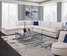 a living room with white furniture and blue accents in front of large windows overlooking the city