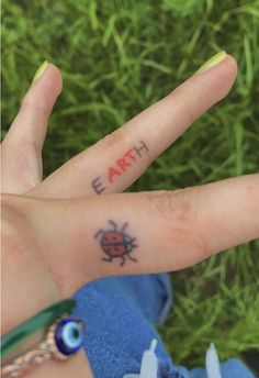 a person's hand with the word earth written on it and a ladybug tattoo