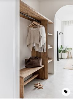 an open closet with clothes and shoes hanging on the wall, next to a wooden bench