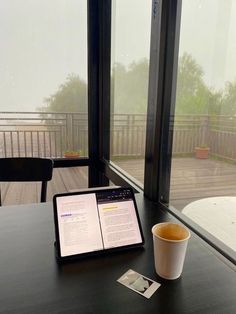 an open book sitting on top of a wooden table next to a cup of coffee