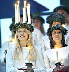 a group of women in white dresses holding candles with their faces covered by wreaths