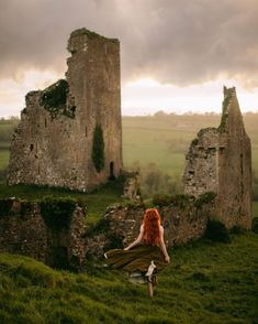 a woman with red hair is sitting on the grass in front of an old castle