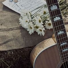 a guitar and some flowers sitting on the ground next to sheet music with white daisies