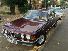 an old car is parked on the side of the road next to a curb with fallen leaves