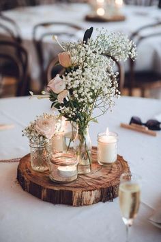 white flowers are in mason jars on a wood slice at a wedding reception centerpiece