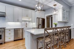 a kitchen with white cabinets and stainless steel appliances in the center island, surrounded by bar stools