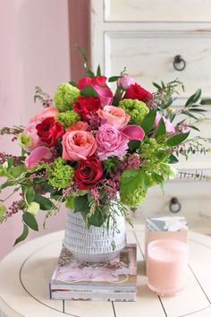 a vase filled with pink and red flowers on top of a table next to a candle