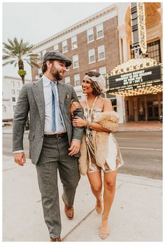 a man and woman are walking down the street in front of a movie marquee