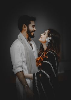 a man and woman standing next to each other in front of a dark background,