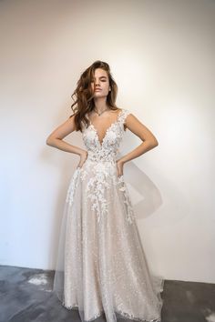 a woman in a wedding dress standing against a white wall with her hands on her hips