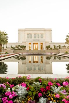 a large building with flowers in front of it and water reflecting on the ground next to it