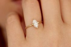 a woman's hand wearing a gold ring with a white stone on it and a diamond in the middle