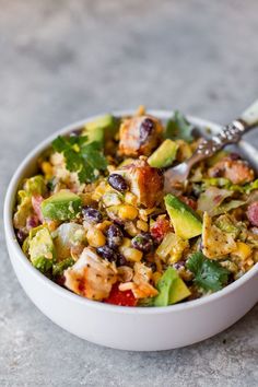 a bowl filled with chicken, black beans and avocado salad next to a fork