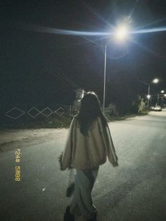 a woman walking down the street at night with her hair blowing in the wind,