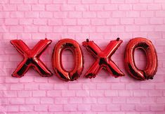 the wordox spelled out in large red balloons against a pink brick wall with an air filled balloon