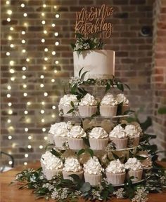 a wedding cake with cupcakes and greenery on top