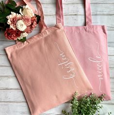 two pink bags with white writing on them sitting next to some flowers and greenery