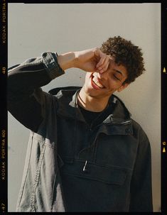 a young man is smiling and holding his hand to his face while standing against a wall