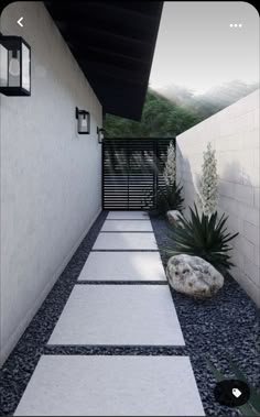 an outdoor walkway leading to a house with white walls and black roofing, surrounded by gravel