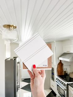 a woman holding up some white tiles in her kitchen