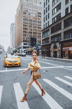 a woman crossing the street in front of taxi cabs on a city street with tall buildings