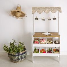 a small wooden stand next to a potted plant on the floor and a wall hanging above it