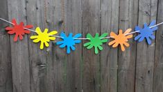 colorful paper flowers are hanging from a string on a wooden fence, with grass in the foreground