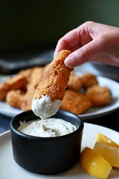 a person dipping something into a small bowl on a plate with lemon wedges next to it