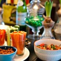 several bowls of food on a table with glasses and bottles in the backgrouf