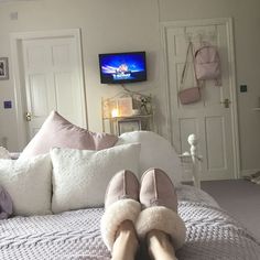 a person's feet in slippers on a bed with white sheets and pillows