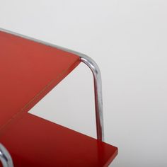 a red chair sitting in front of a white wall next to a metal frame on the floor