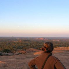 a person sitting on top of a hill looking out at the sky and land below