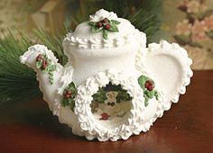 a white tea pot decorated with holly wreaths and an owl in the center on a wooden table