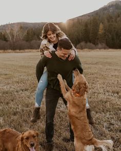 a man and woman are playing with their dogs in the field while the sun is setting