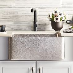 a kitchen sink sitting under a faucet next to a counter top with flowers in it