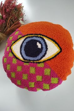 an orange and pink round pillow with eye on it next to dried flower bouquets