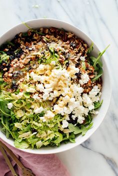 a white bowl filled with salad on top of a pink napkin next to utensils