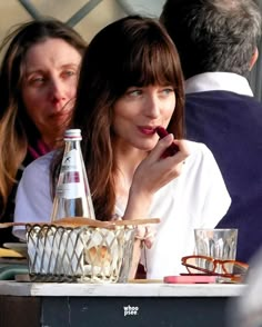 a woman sitting at a table with a bottle of water in front of her face